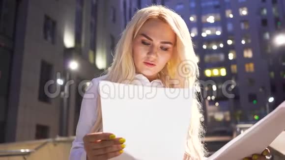 金发自信的女商人站在街上晚上翻阅报纸微笑女工视频的预览图