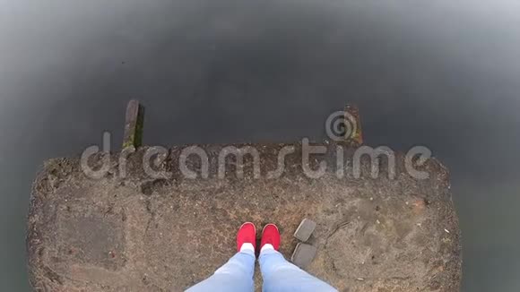 穿着蓝色牛仔裤和红色鞋子的女孩站在海滨的石头混凝土码头上视频的预览图