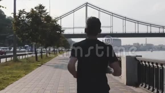 后侧跟随年轻活跃男子在城市码头沿河奔跑精力充沛的肌肉男孩跑得很快运动员跑步视频的预览图