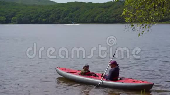 一个年轻人和他的小儿子坐在湖或海湾里的一艘充气大皮艇上视频的预览图