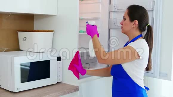 年轻漂亮的女人站在一边用洗涤剂洗了一个冰箱把洗涤剂涂在冰箱上视频的预览图