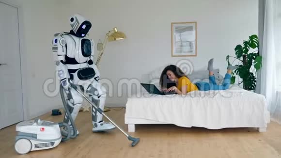 女孩用笔记本电脑工作而一个机器人真空清洁机器人和人类的合作视频的预览图