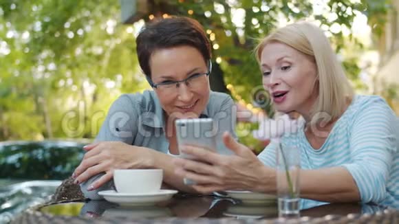 漂亮女人在露天咖啡馆里用智能手机慢动作微笑视频的预览图