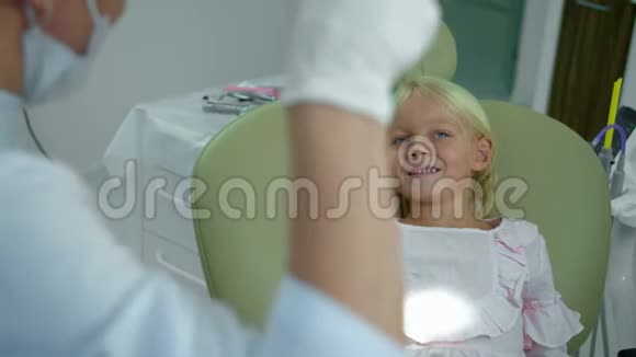 女牙医用灯照着女孩的嘴看着她的牙齿视频的预览图