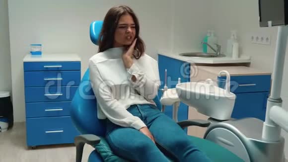 年轻漂亮的黑发女人病人坐在牙医办公室时觉得牙痛碰到她的脸颊视频的预览图