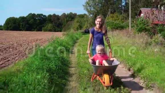 爱的女人推着手推车和快乐的小女孩穿过村庄视频的预览图