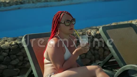 一位年轻女子坐在游泳池旁的躺椅上喝奶昔视频的预览图