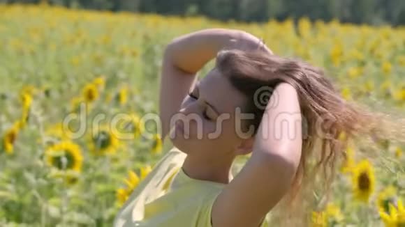 肖像一位留着长发的美丽女子站在一片向日葵的田野里放松头发在风中撕裂视频的预览图