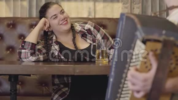 不可辨认的男人演奏手风琴而迷人的丰满女人喝啤酒送他空气亲吻概念视频的预览图