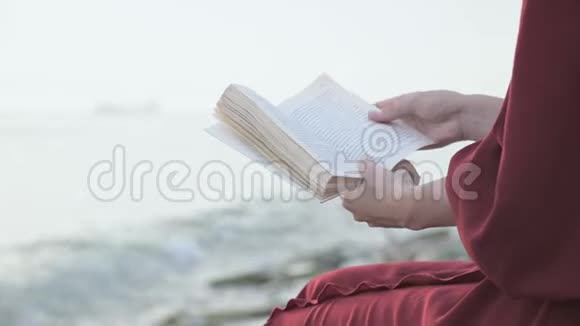 穿着红色衣服的女孩后面的景色在海边看书双手特写视频的预览图