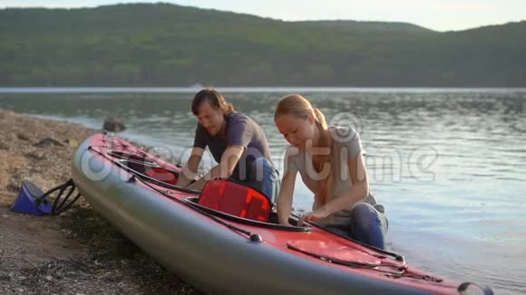 年轻的男人和女人准备他们的充气皮艇在湖或海中划水慢镜头视频的预览图