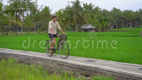 一个年轻人骑着自行车穿过美丽的稻田前往东南亚的概念慢镜头视频的预览图