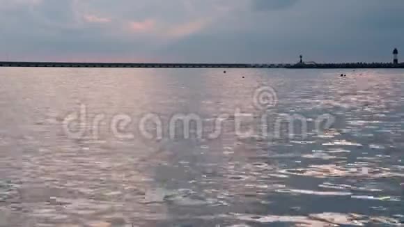夏季日落时海水平静海面上阳光反射地平线上有小浪码头和灯塔视频的预览图