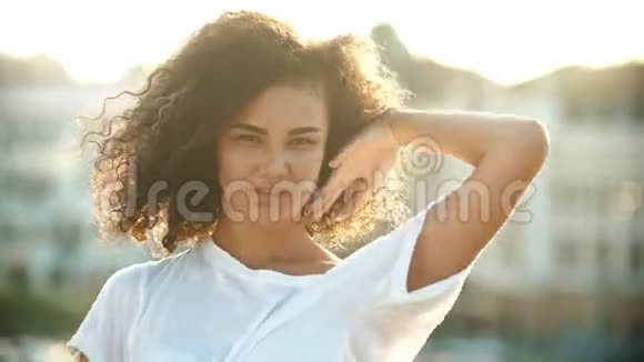 一个年轻迷人的女人在城市背景上玩弄她的卷发表演性感的舞蹈明亮的日落视频的预览图