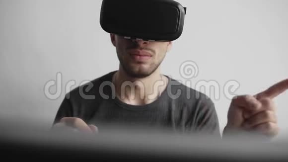 年轻人使用虚拟现实护目镜耳机坐在办公室里对着电脑试图触摸视频的预览图
