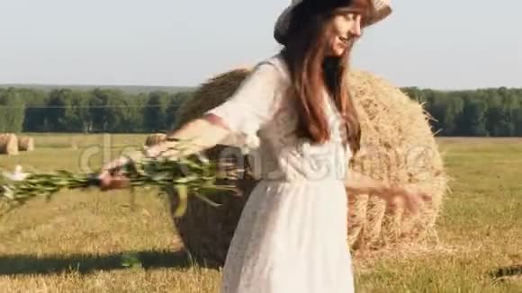 戴着草帽戴着鲜花的年轻女子在草地上旋转视频的预览图