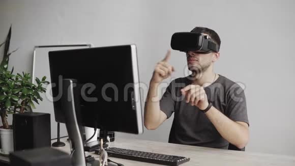 年轻人使用虚拟现实护目镜耳机坐在办公室里对着电脑试图触摸视频的预览图