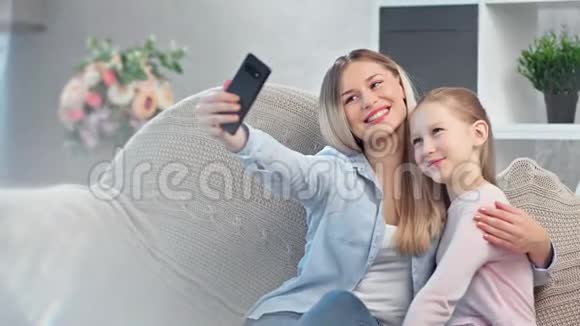 快乐的年轻妈妈和十几岁的女儿在家里玩智能手机自拍视频的预览图