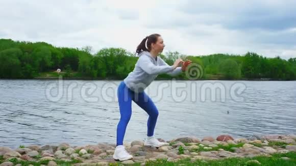 一位身材苗条的女士穿着时尚运动服装在河边蹲着视频的预览图