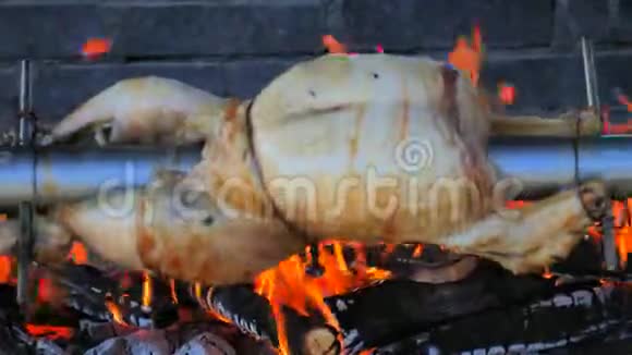 接近旋转烤鸡在不锈钢梁上接近暗红色火焰鸡下面的干沙刺油视频的预览图