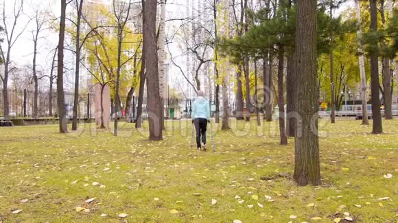 女人在秋天的公园里练习北欧行走她离开相机地上秋天的黄叶视频的预览图