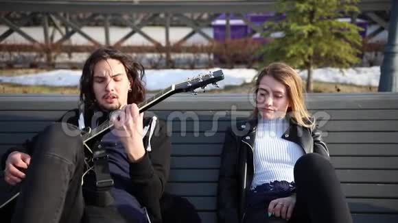 年轻夫妇躺在长凳上一个男人弹吉他他的女朋友听他说话视频的预览图