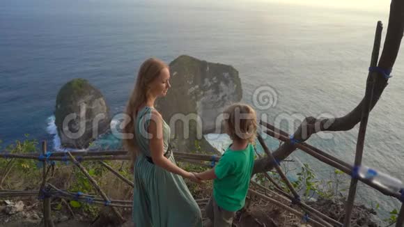 年轻女子和她的小儿子游客参观了在NusaPenidaKelingking海滩的所谓暴龙岩视频的预览图