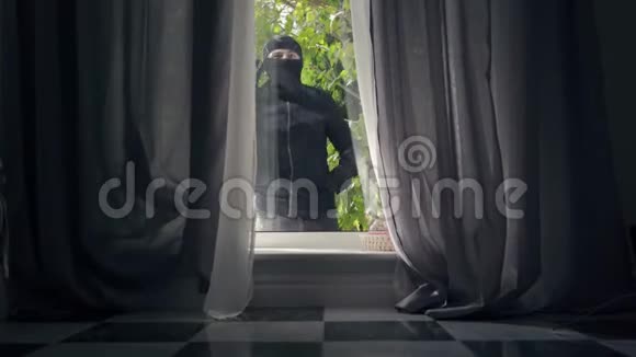 穿着黑色衣服和巴拉克拉瓦的年轻小偷正看着窗户准备闯入房子犯罪概念视频的预览图