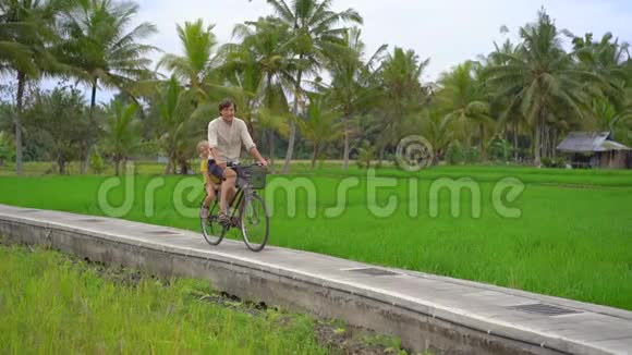 一个年轻人和他的小儿子骑着自行车穿过美丽的稻田前往东南亚构想视频的预览图
