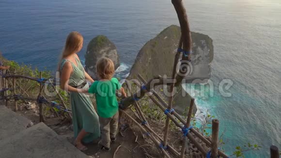 年轻女子和她的小儿子游客参观了在NusaPenidaKelingking海滩的所谓暴龙岩视频的预览图