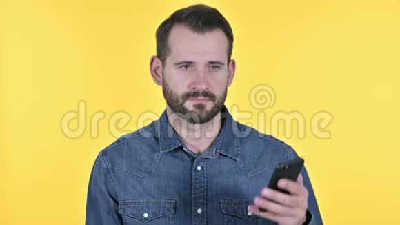 开朗的胡子年轻人在智能手机上交谈黄色背景视频的预览图