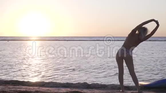 穿比基尼的金发少女站在沙滩上伸展着夕阳西下视频的预览图