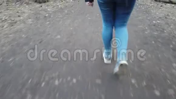 一个穿着蓝色牛仔裤和运动鞋的女孩正走在森林里特写着她的脚女游客散步视频的预览图
