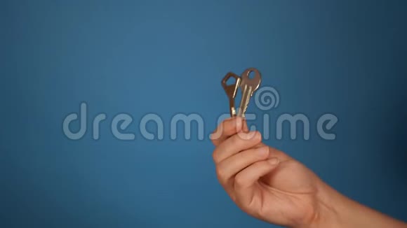 用不同的钥匙特写手女人手拿着蓝色背景上的两把钥匙视频的预览图