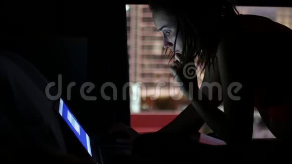 在黑暗中工作在笔记本电脑上的女人一扇窗户背景上的剪影可以看到夜城视频的预览图