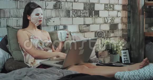 一位商务女性在床上躺着手提电脑上戴着面罩这是一种晨间美容习惯视频的预览图