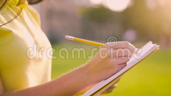 特写女性手女人在日落背景上用铅笔在笔记本上写字4K视频的预览图