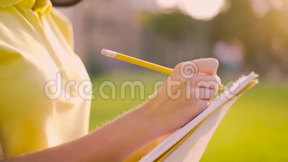 特写女性手女孩用铅笔在笔记本上用柔和的背光做笔记4K视频的预览图