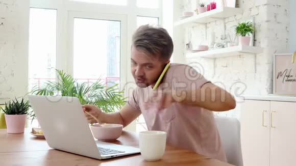 忙碌的年轻人在吃早餐使用他的笔记本电脑和智能手机视频的预览图