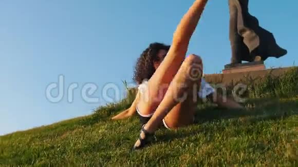 迷人的瘦骨嶙峋的穆拉托女人躺在草地上表演脱衣舞舞蹈改变她的腿视频的预览图