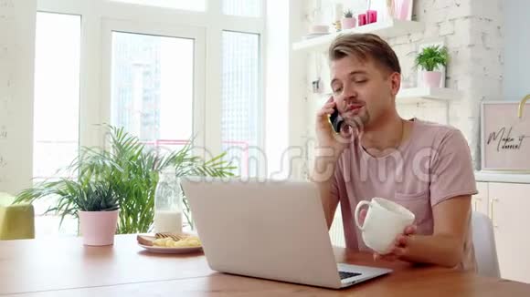 年轻人在厨房里吃早餐用笔记本电脑和智能手机视频的预览图