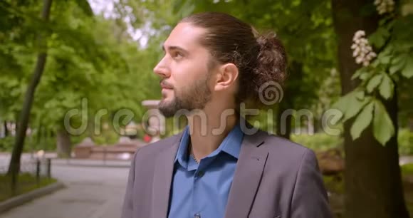 英俊的时髦男人穿着正式西装扎着马尾辫在公园里欢乐地对着镜头微笑视频的预览图