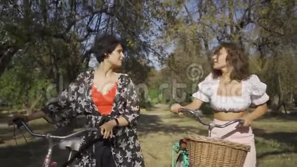 两个可爱的年轻女朋友在户外散步女孩子在狭窄的路上骑自行车时说话视频的预览图