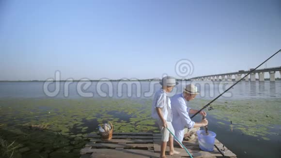一家人钓鱼码头上有爱心的父亲教他心爱的小男孩在钓鱼的时候把河里的钩鱼从钩子上移开视频的预览图