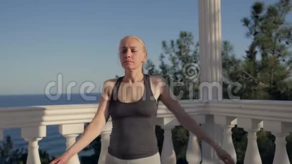 运动的女人站在露台上白色的柱子俯瞰大海做体操视频的预览图