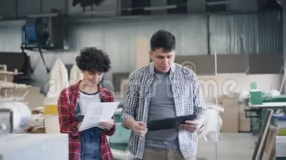 女孩和男孩走在木头车间里拿着平板电脑和纸文件说话视频的预览图