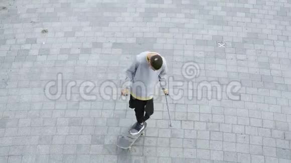 俯视的年轻人一条腿拄着拐杖在滑板上旋转做着花样残疾人培训视频的预览图