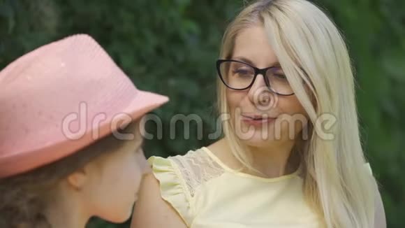 肖像成熟的金发母亲戴着眼镜她的小女儿坐在夏天公园的长凳上说话视频的预览图