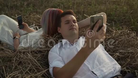 男人和女人躺在干草堆上看智能手机视频的预览图
