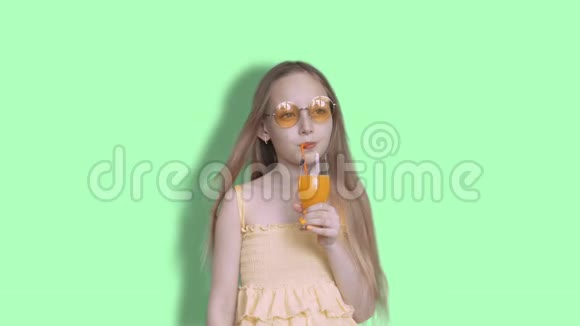 体贴的女孩在工作室里用玻璃吸管喝橙汁戴着黄色太阳镜的少女视频的预览图